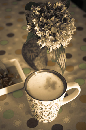 A cup of hot coffee with milk, flowers, honey and book. Romantic background with retro filter effectの写真素材