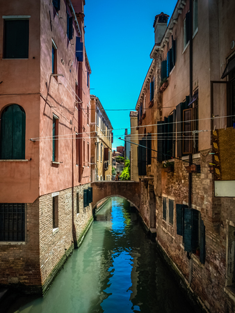 Colorful narrow lateral canal and pedestrian bridge at morning, in Venice, Italiaの写真素材