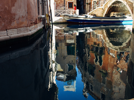 Colorful narrow lateral canal and pedestrian bridge and their reflection at morning, in Venice, Italiaの写真素材
