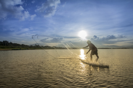 A man throwing fishing net during sunriseの写真素材