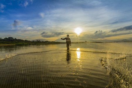 A man throwing fishing net during sunriseの写真素材