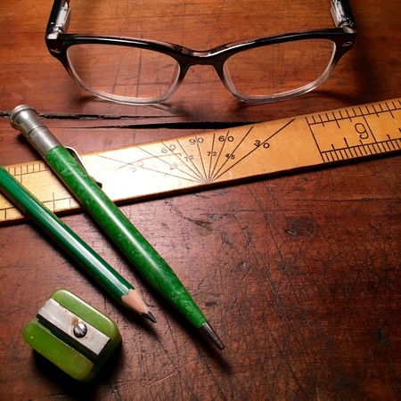 Ruler, writing utensils and spectacles on wooden desktop.