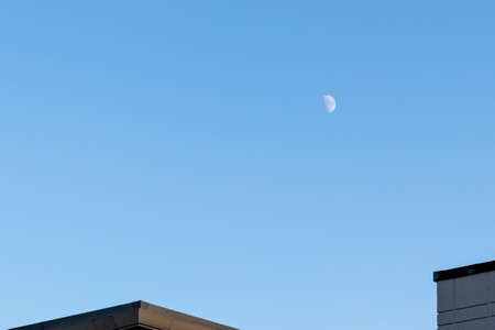 Half moon floating in the blue sky above the residential areaの写真素材