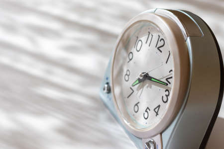 A table clock on a desk by the window in the morningの写真素材