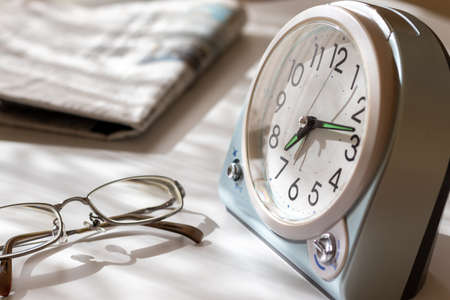 Eyeglasses, table clock and newspaper on a desk by the window in the morningの写真素材