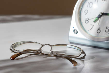 Table clock and eyeglasses on a desk by the window in the morningの写真素材