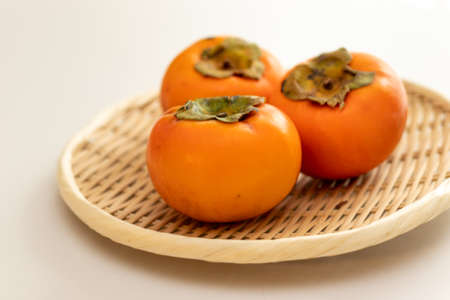 Delicious orange persimmons on a bamboo colanderの写真素材