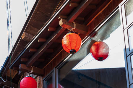 Japanese red lanterns hanging from the eaves of a wooden houseの写真素材