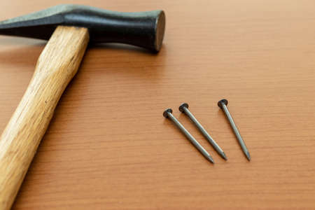 Three iron nails and a hammer on the wooden board