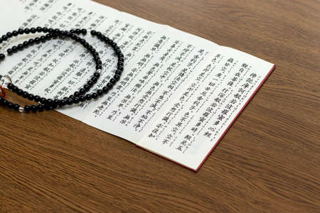 Buddhist sutra and rosary on a wooden deskの写真素材