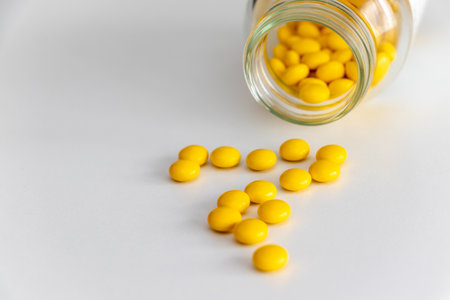 Yellow pills spilled on the table from a toppled glass bottleの写真素材