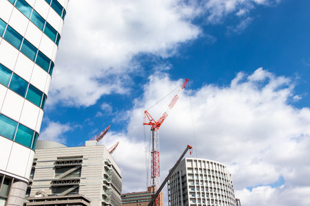 Modern office building with construction cranes on a background of blue skyの写真素材