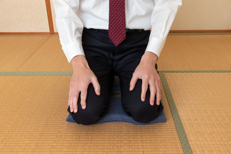 A man in a white shirt sitting on a cushion in a Japanese-style room with tatami flooringの写真素材