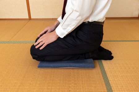 A man in a white shirt sitting on a cushion in a Japanese-style room with tatami flooringの写真素材