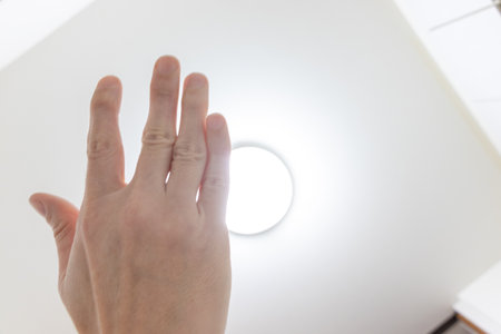 Hand blocking the bright light from the ceiling lightの写真素材