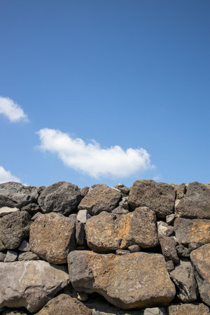 Old stone wall with blue sky and white clouds in the background.