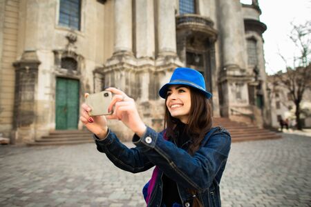 Smiling young girl taking pictures of the architectural monuments of the old city Lviv. Ukraine.