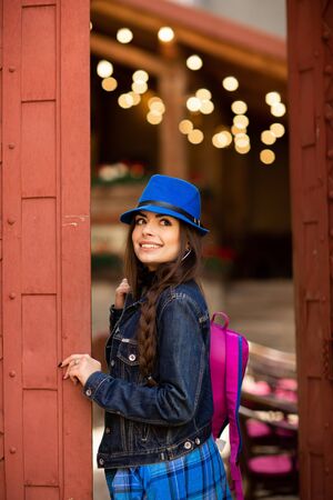 Smiling pretty girl in blue hat near old building with antique red doors. Female model posing.の写真素材