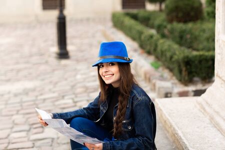 A young woman sits on the stairs in the old courtyard, and reads the map. Lviv, Ukraine.の写真素材