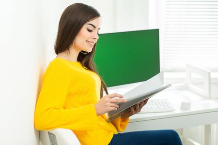 Young woman sitting at workplace and reading paper in office. On the background is a green screen.の写真素材