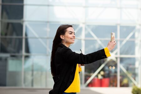 Cheerful brunette woman in yellow sweater making sefie against airport background. Modern technology.の写真素材