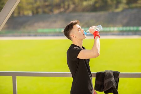Fitness man drinking water on the background of green grass. Thirsty athlete having cold refreshment drink after intense exercise.の写真素材