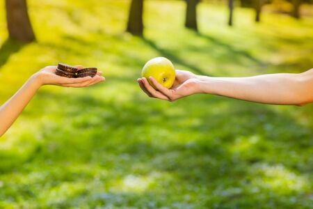 Two hands, female and male, holding and comparing cookie and apple. Background of the green park.の写真素材