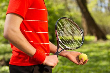 Close up of men's hands hold a tennis racket and ball on the green background. Sport concept.の写真素材