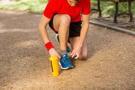 Handsome young runner tying shoelaces on the track in the spring park. Near him is an orange thermocouple.の写真素材