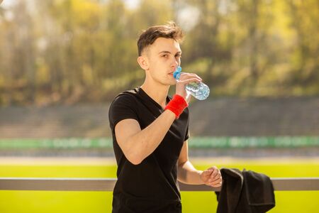 Fitness man drinking water on the background of green grass. Thirsty athlete having cold refreshment drink after intense exercise.の写真素材