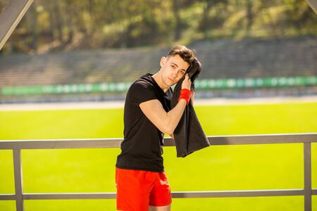 Young sporty man resting and wiping his sweat with a towel after workout sport exercises outdoors on the background of green grass.の写真素材