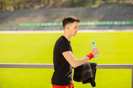 Fitness man drinking water on the background of green grass. Thirsty athlete having cold refreshment drink after intense exercise.の写真素材
