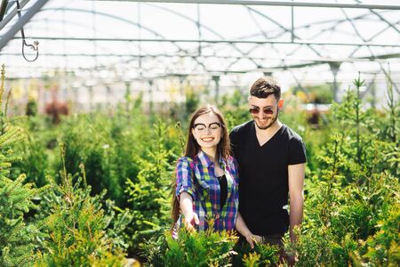 Young couple, man and woman, standing together in the garden center and choose plants for greening the house.の写真素材