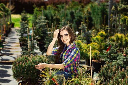 Pretty woman choosing and buying green plants for the garden. Beautiful girl keeping it with hands and enjoying the beauty.の写真素材