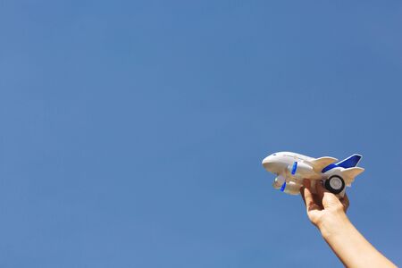 Woman's hands holding a white and blue children's airplane. Blue sky background. Little toy plane. Reaching goals. Dreams of traveling after coronavirus quarantine.の写真素材