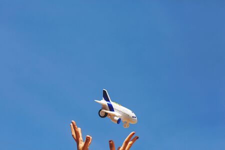 Woman's hands throws in the air a white and blue children's airplane. Dreams of traveling during a coronavirus quarantine. Blue sky background. Copy space.の写真素材
