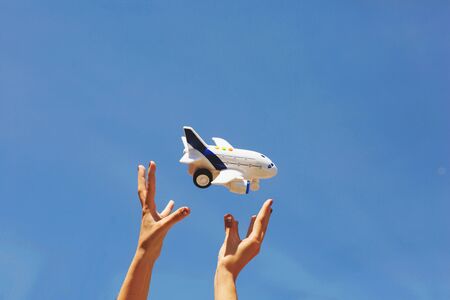 Women's hands throw white and blue children's airplane. Blue sky background.の写真素材