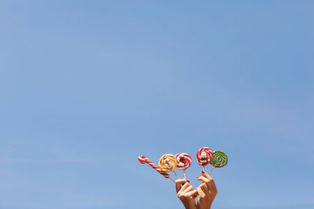 Womens hands holding colored Christmas candies on the blue sky background. Space for text. On the sweets is depicted snowman and Santa, Christmas concept.の写真素材