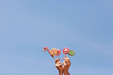 Womens hands holding colored Christmas candies on the blue sky background. Space for text.の写真素材