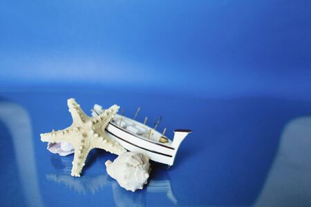 White little toy ship with shells on a blue background.の写真素材
