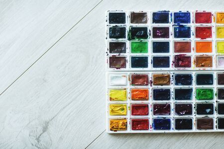 A box of colored watercolor paints on the background of a wooden floor, located on the side of the photo. Space for text.の写真素材