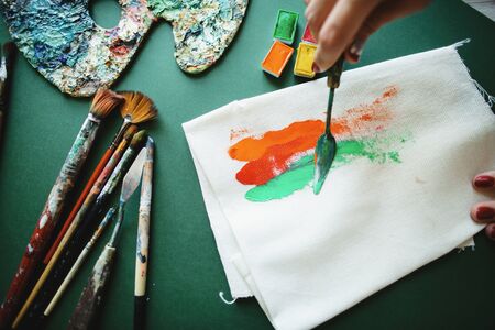 Creative disorder in the work environment. The artist smears with palette knife orange, red and green paints on the canvas.の写真素材