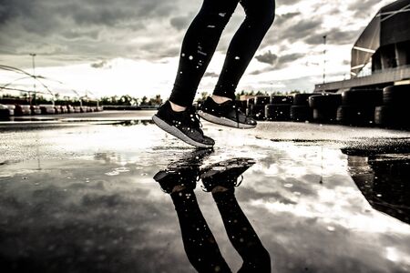 Sports background. Strong athletic legs of a woman runner in motion. Morning workouts outdoors after the rain. Woman preparing for a marathon.の写真素材