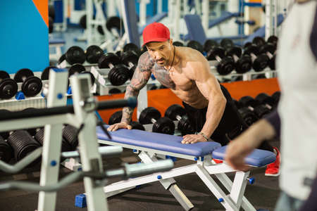 Strong sporty man doing push-ups on bench during workout in gym.