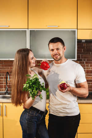 Young attractive couple standing in the kitchen. Man and woman holding vegetables and fruits. Healthy food concept. Diet for family, healthy lifestyle.の写真素材