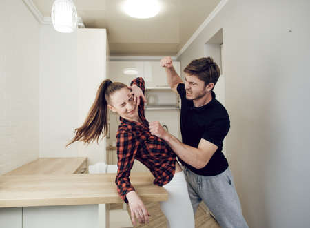 Domestic violence concept and alcoholism. Problems of a young family. The man shouts at the woman and threatens with a fist. A frightened young woman cryingの写真素材