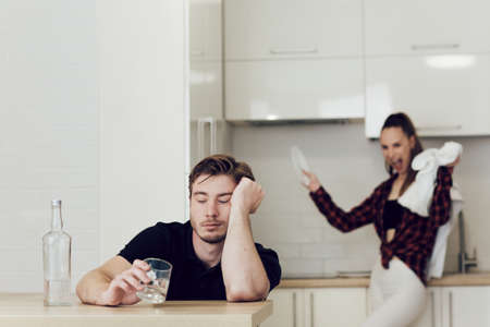Drinking problem drunk man in a young family. A man drinks while sitting at a table in the kitchen,...