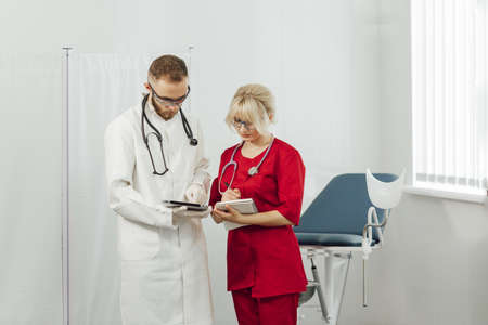 Male and female medical doctors using a tablet and write something and a notebook in a hospital office. Doctors in uniform, man and woman in a gynecological officeの写真素材
