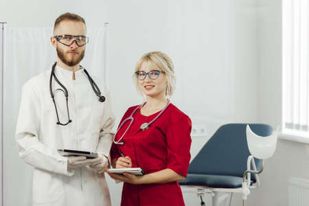 Close up portrait of two medical doctors standing in a hospital office and looking at camera. Doctors in uniform, man and woman in a gynecological officeの写真素材