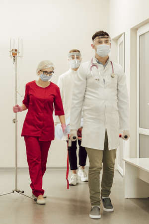 A team of doctors carry a sick patient on a stretcher. Ambulance doctors in protective masks and suits, the patient suspects coronavirus. The work of medics during a pandemicの写真素材
